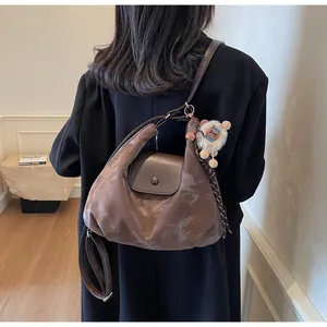 Braune glänzende Hobo-Tasche mit süßem Schaf-Plüsch-Anhänger an einem Modell