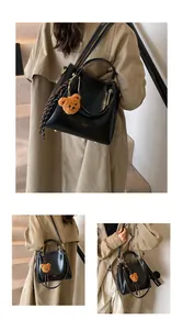 Detail of black leather handbag with bear charm and decorative scarf in street style view