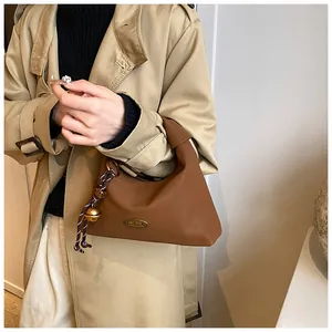 Detalle de bolso sobaquero de cuero marrón con asa de nudo y placa de metal hecha