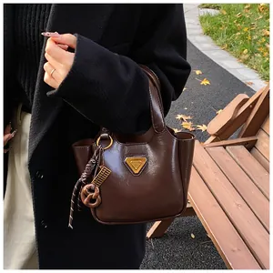 Close-up of glossy brown bucket bag with golden triangle logo and pretzel charm accessory