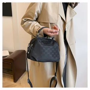 Détail d'un sac bandoulière en nylon noir avec monogramme EB porté sur un trench coat