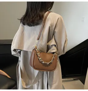 Détail d'un sac bandoulière marron en cuir grainé avec une grosse chaîne dorée sur un trench