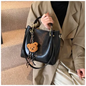Detail of black glossy handbag with gold metal handle and brown plush bear charm