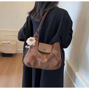 Detail der dunkelbraunen, glänzenden Hobo-Tasche mit einem weißen Plüschlamm-Anhänger