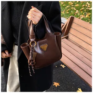 Detailed view of deep brown glossy leather bucket bag with metallic logo and unique charms