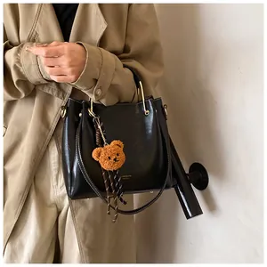 Detail of black glossy leather bucket bag with gold handle and bear charm on trench coat