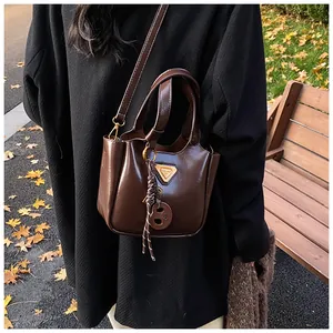 Detail view of coffee brown bucket bag with shiny leather texture and round charm