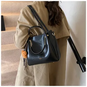 Detail of black matte handbag with gold ring handles, plush charm and ribbon detail
