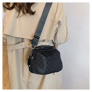 Détail du sac à bandoulière en nylon noir avec motif lettré sur un trench-coat
