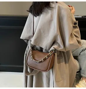 Détail du sac bandoulière marron foncé avec chaîne dorée sur un trench-coat kaki
