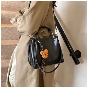 Detail of black leather bucket bag with gold hardware and plush bear charm on model
