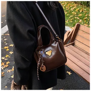 Close-up of gloss dark brown bucket bag with gold triangle logo and woven rope charm
