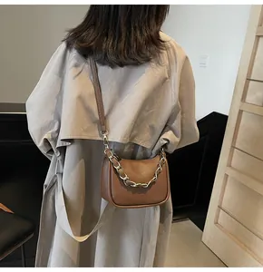 Sac bandoulière en cuir marron avec chaîne dorée porté sur un trench-coat beige élégant