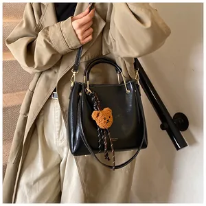 Detail of black faux leather tote bag with gold metal handle and plush bear charm decoration