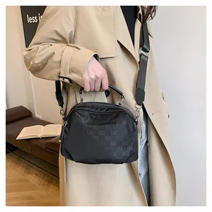 Détail du sac bandoulière en nylon noir avec logo, poignée anneau métal et large sangle