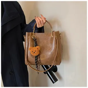 Detail of a brown leather bucket bag with gold handle and a cute plush bear charm