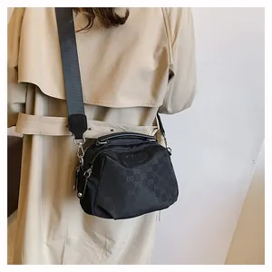Détail de la bandoulière en nylon noir portée avec un trench-coat beige élégant