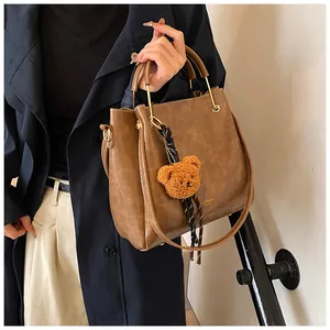 Brown PU leather handbag with plush bear charm and silk scarf detail shown on model