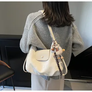 Detailansicht der cremefarbenen Hobo-Tasche mit Löwen-Plüschanhänger am Modell getragen