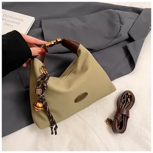 Detalle de bolso medialuna de nailon caqui con etiqueta de cuero y colgante trenzado
