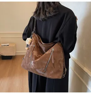 Detail of a large brown leather tote bag with silver zippers and a cute plush bear keychain