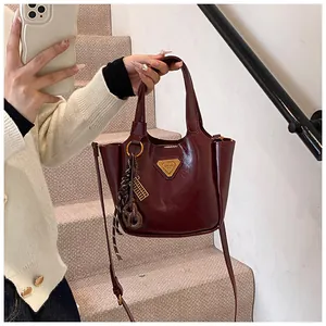 Close-up of a burgundy patent leather bucket bag with metallic triangle logo and strap
