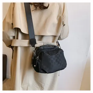 Sac bandoulière en nylon noir avec motif monogramme porté sur un trench-coat kaki
