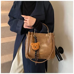 Detail of vintage brown PU leather bucket bag with plush bear charm and striped ribbon strap