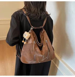 Detail of a brown PU leather tote bag with metallic zippers and a plush charm on the back