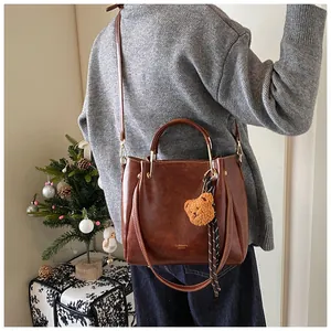 Detail of dark brown leather tote bag with plush bear charm and silk scarf decoration