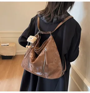 Back view of a minimalist brown glossy triangle tote bag with plush charm and silver zippers
