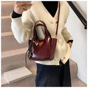 Detail of burgundy glossy bucket bag with metal triangle logo and quirky charm pendants