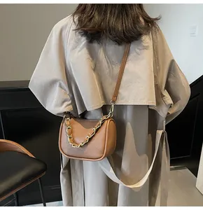 Sac bandoulière en cuir marron avec chaîne dorée porté par un mannequin en extérieur