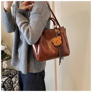 Close-up of brown oiled leather tote bag with brand lettering and a cute bear charm