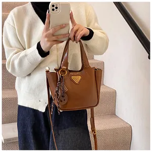 Close-up of brown bucket bag featuring gold triangular logo and woven charm detail