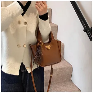 Close-up of brown leather bucket bag featuring a gold triangle logo and silk scarf detail