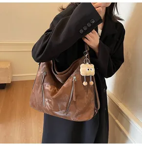 Detail of glossy brown faux leather tote bag with dual zippers and plush bear charm
