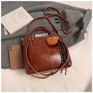Detail of vintage brown oil wax leather tote with cute bear pendant on a grey coat