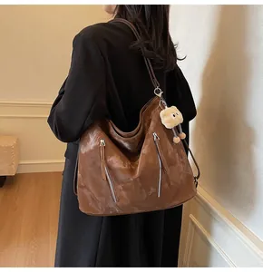 Back view of brown patent leather tote bag with silver zippers and plush charm