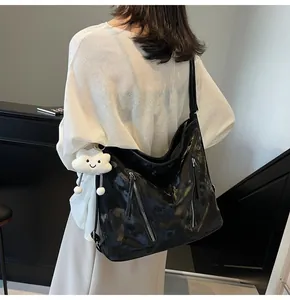 Detail view of black patent leather tote bag with silver zippers and plush white charm