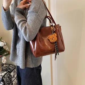 Brown leather tote bag for women with gold logo and plush bear charm on grey sweater