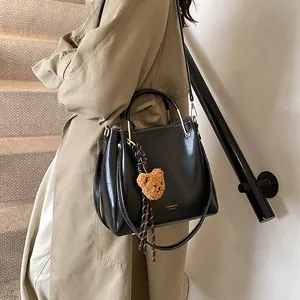Chic black bucket handbag with white contrast stitching and brown plush bear charm