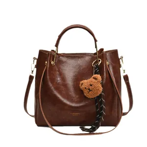 Deep brown faux leather handbag with plush bear charm and striped ribbon on white background