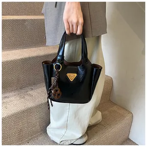Detail of black glossy bucket bag with golden triangle logo and woven pendant charm