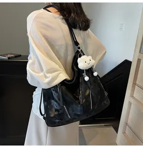 Macro detail of glossy black patent leather tote with silver zippers and plush pendant