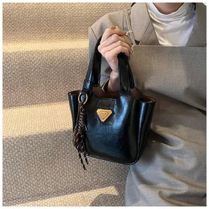 Detail of black glossy bucket bag featuring gold triangle logo and braided rope charm
