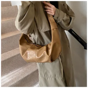 Detail of a brown crescent-shaped pleated bag with soft faux leather texture and wide strap