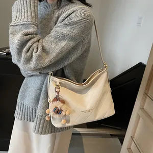 Sac fourre-tout matelassé en cuir crème avec breloque en peluche porté à l'épaule chic