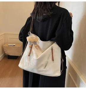 Detail of off-white tote bag with metal zippers, brown straps and a plush bear charm