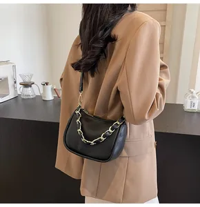 Détail du sac à main noir en cuir grainé avec chaîne dorée porté par un mannequin